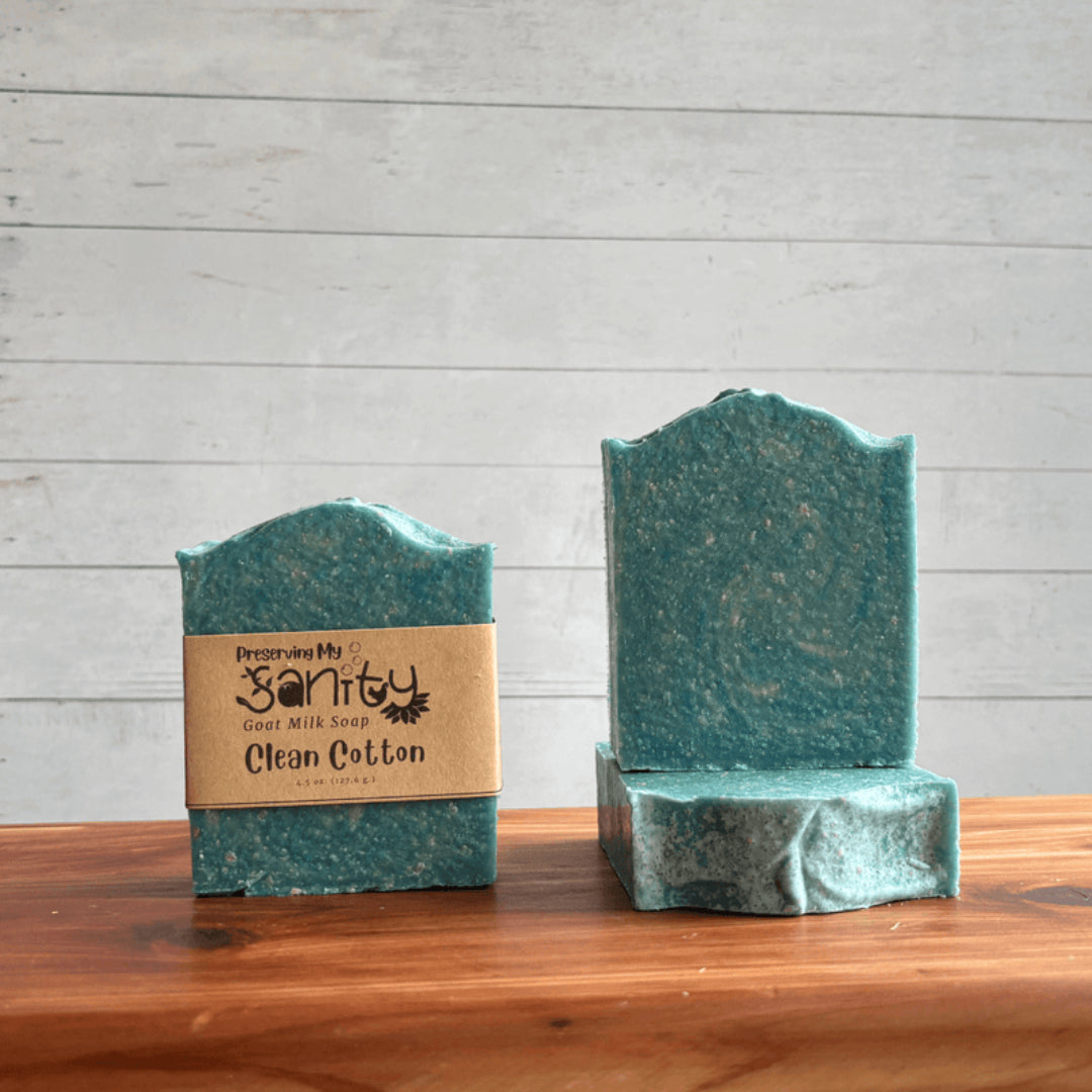 Two bars of green soap called Clean Cotton with a label on a wooden surface and a gray background