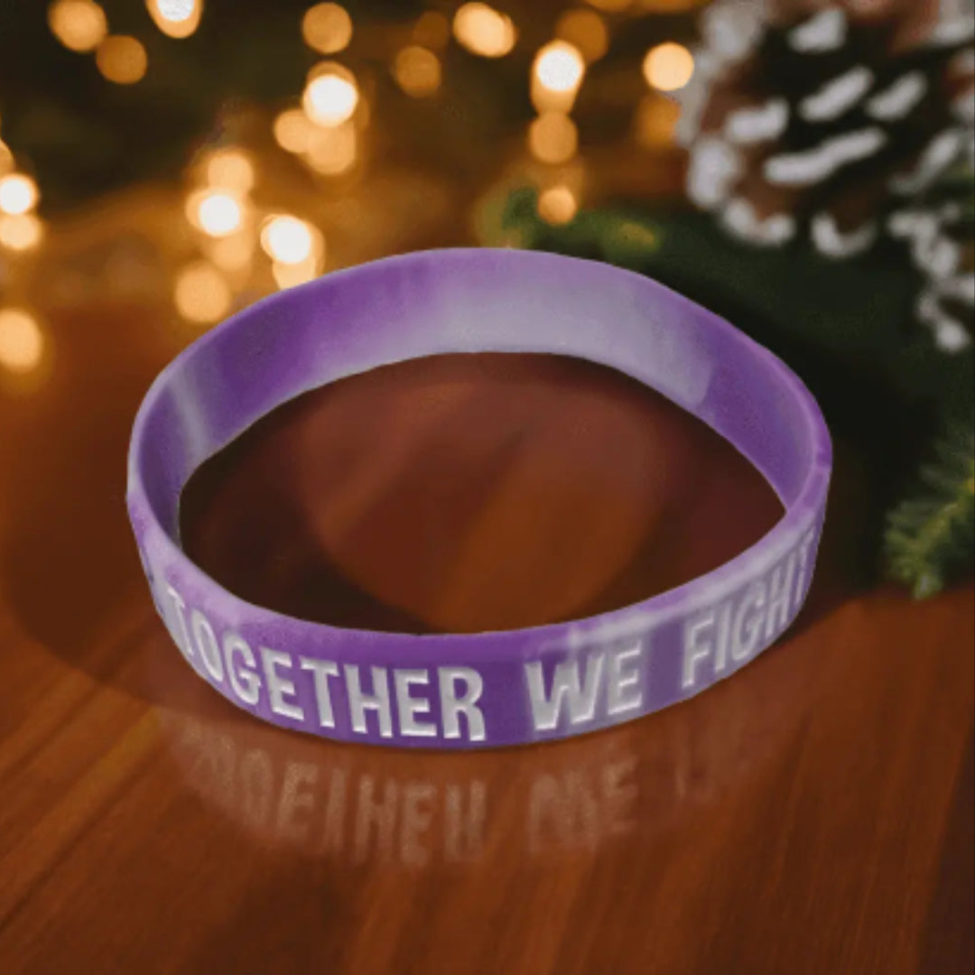 Purple wristband with 'Together We Fight' text on a wooden surface with blurred lights and pine cones in the background.