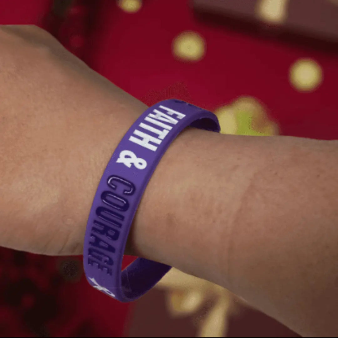 Purple wristband with 'FAITH & COURAGE' text on a wrist against a blurred background