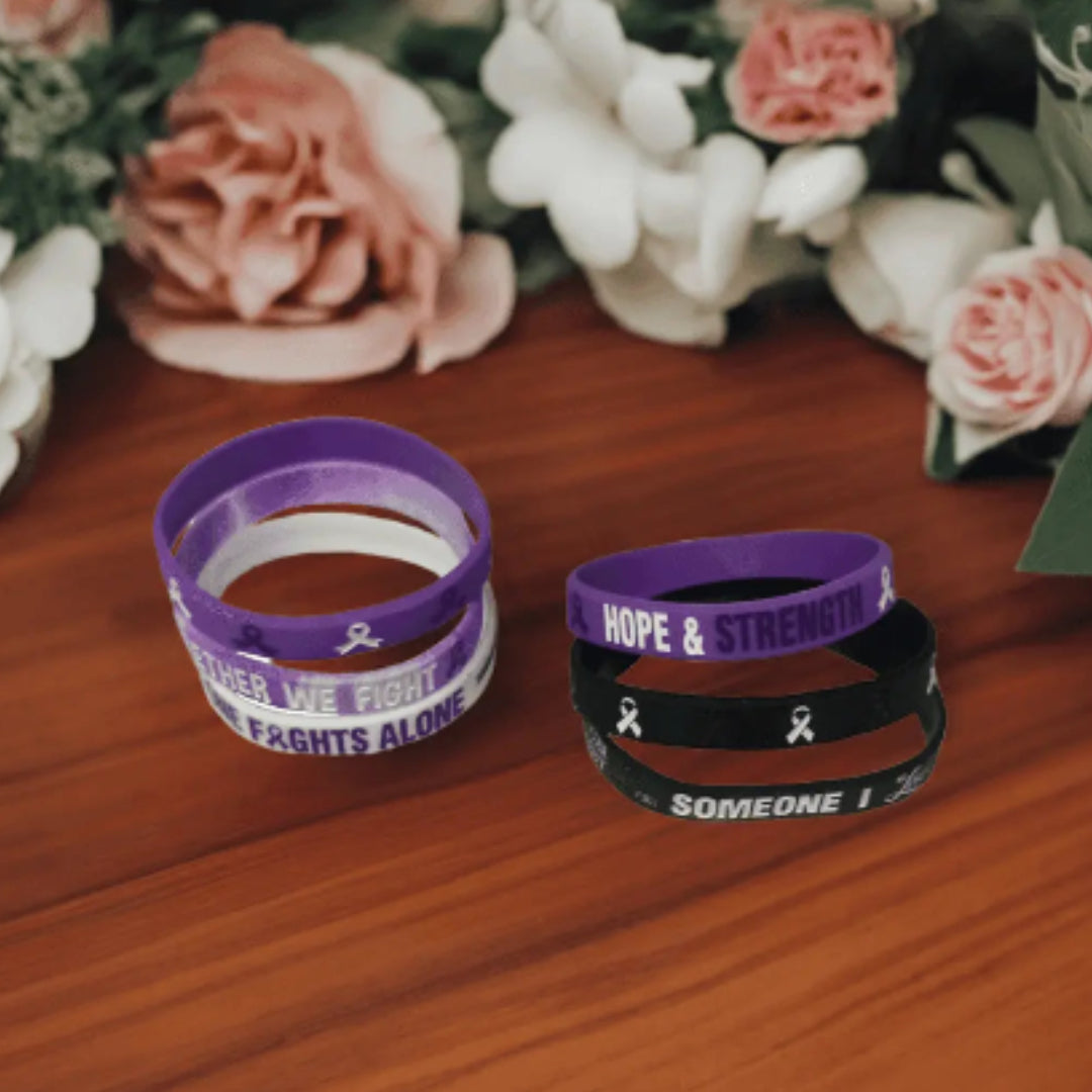 Purple and black wristbands with motivational text on a wooden surface with flowers in the background