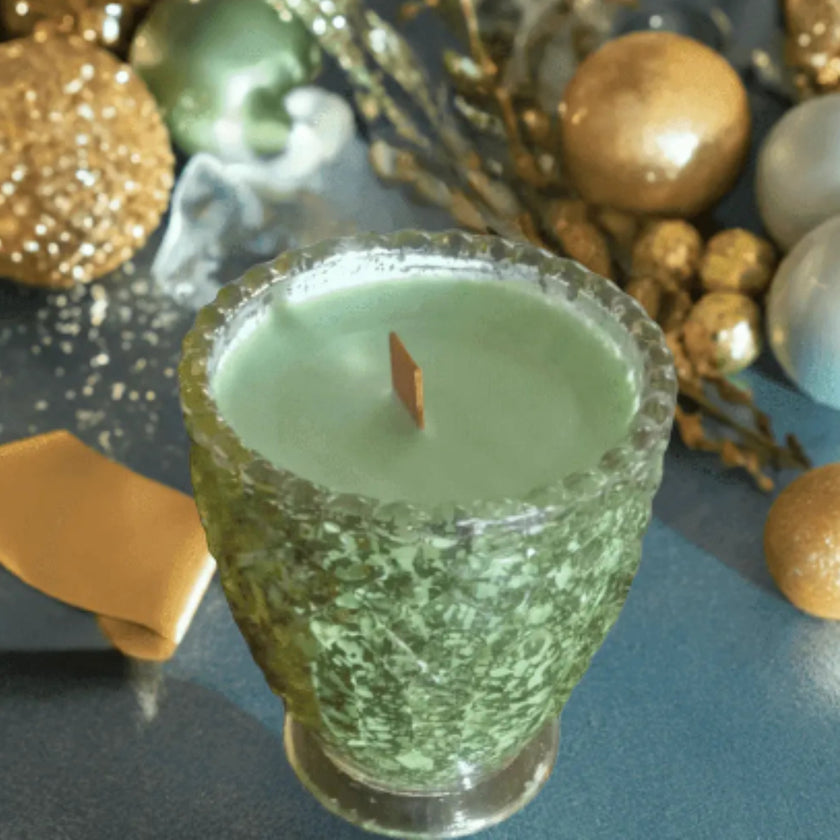 Green candle in a textured glass holder with decorative elements in the background