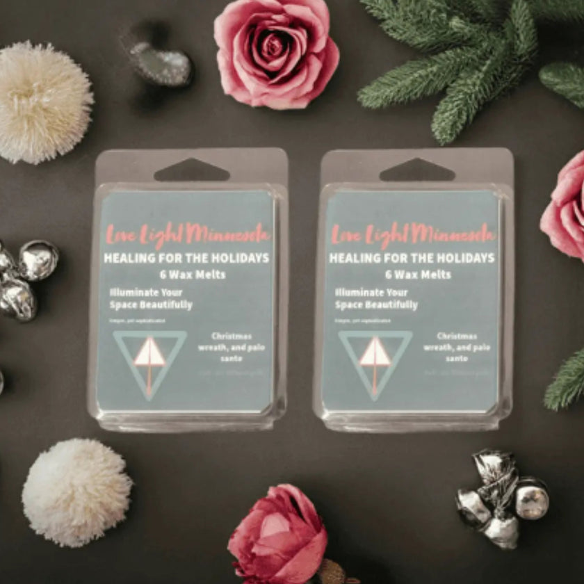 Two packages of 'Healing for the Holidays' wax melts surrounded by decorative elements on a dark surface.
