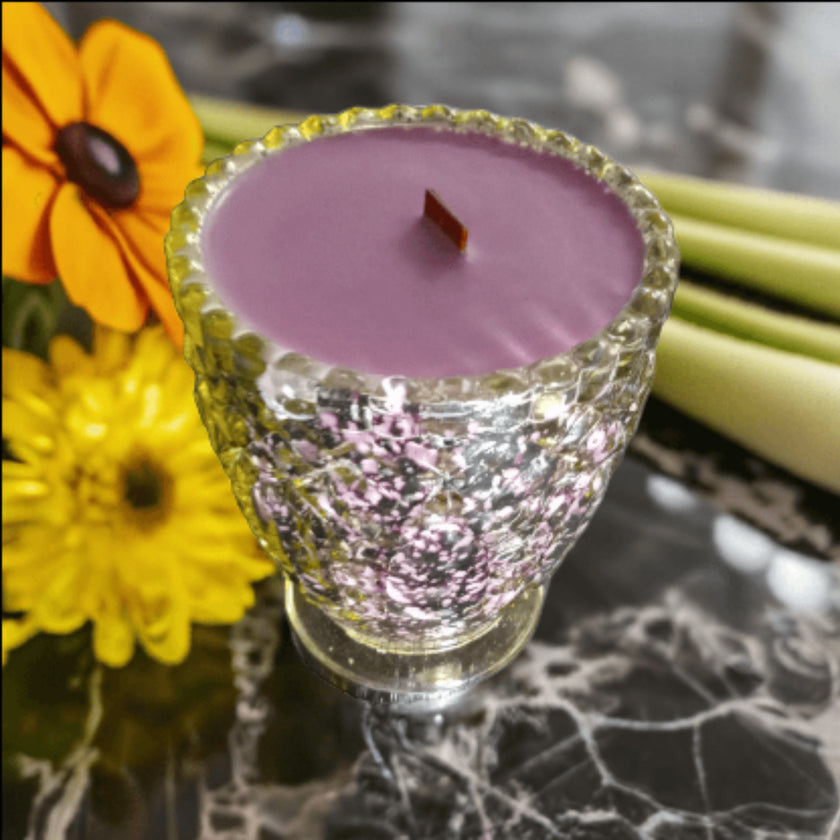 Purple candle in a decorative glass holder with flowers in the background