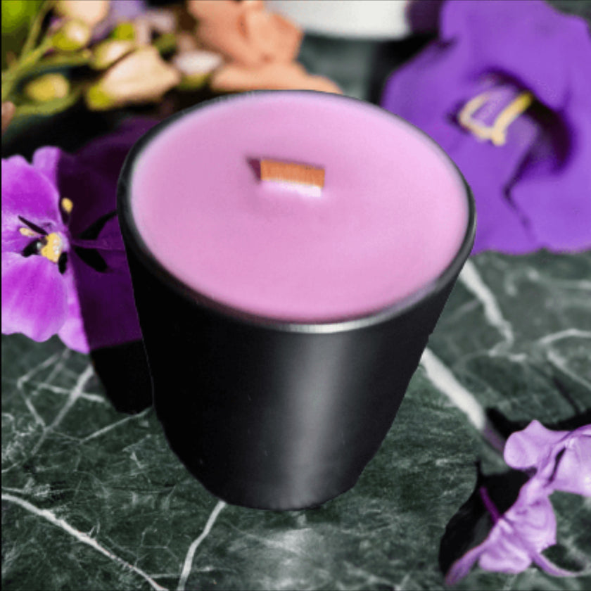 Purple candle in a black holder on a marble surface with purple flowers in the background