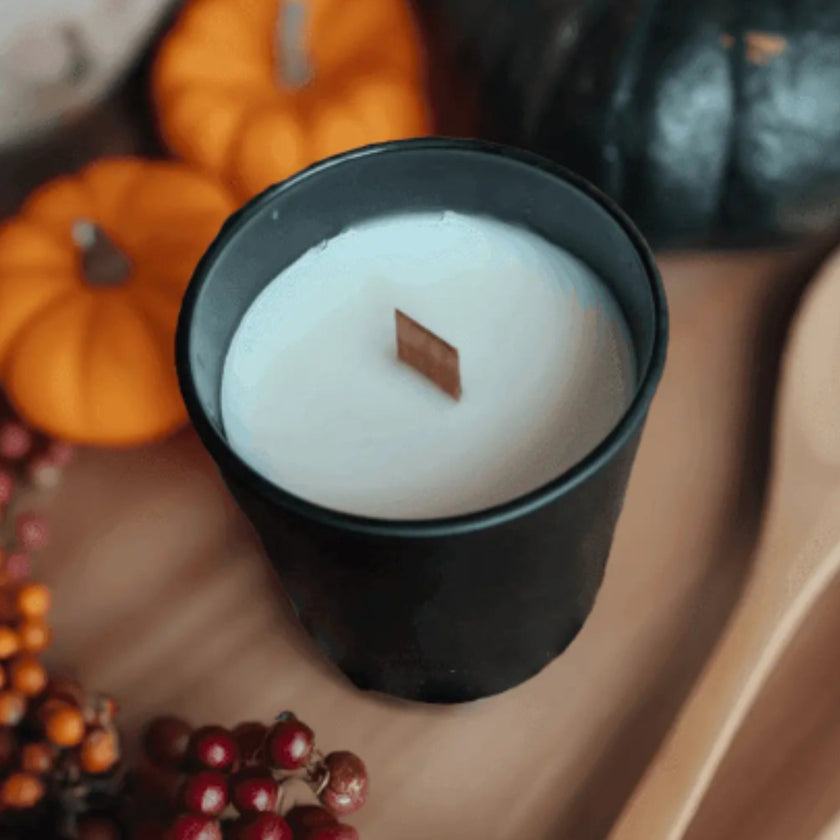 White candle in a black holder with pumpkins and berries on a wooden surface