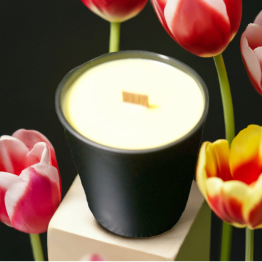 Black candle with a lit wick surrounded by colorful tulips on a dark background