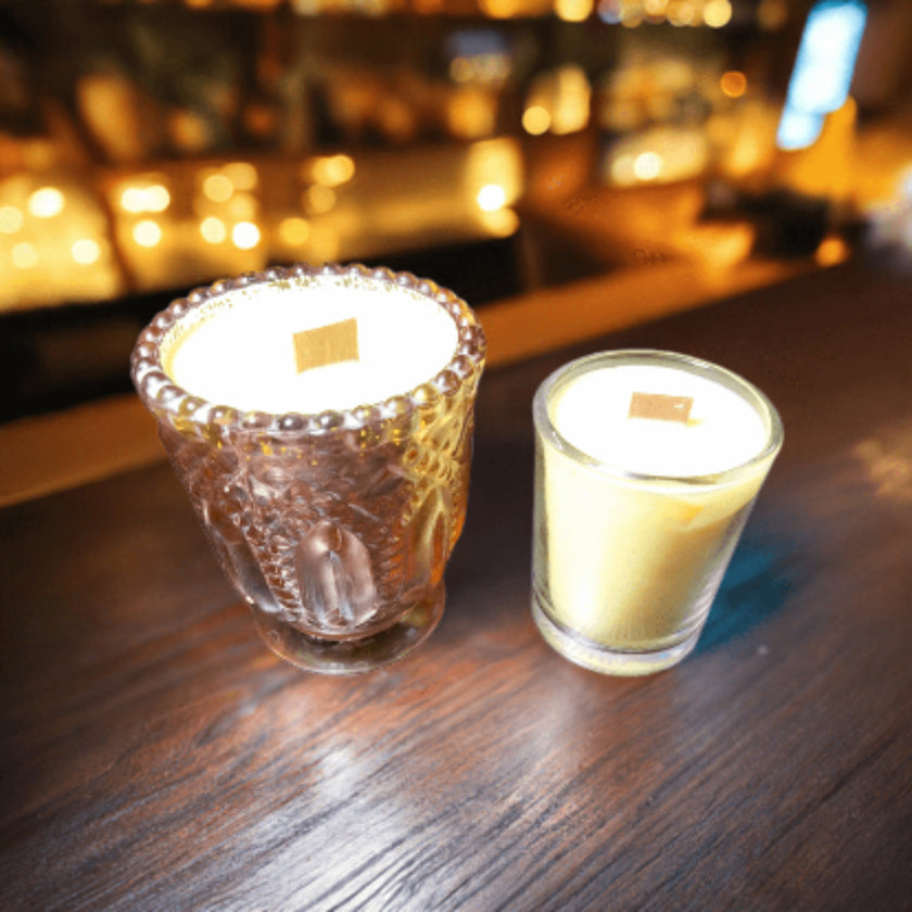 Two lit candles in glass holders on a wooden surface with a blurred bar background.