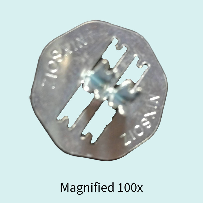 Metallic wick holder with cut-out design on a light blue background, magnified 100x.