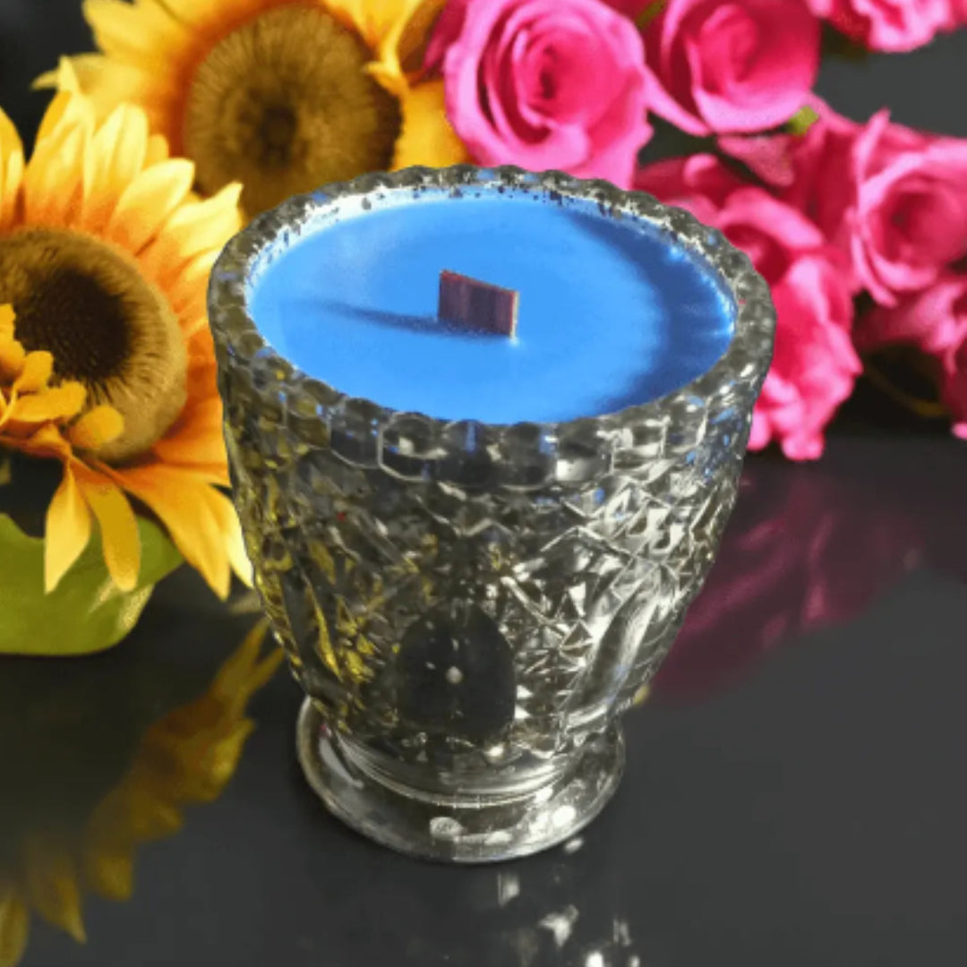 Blue candle in a decorative glass holder with sunflowers and pink roses in the background