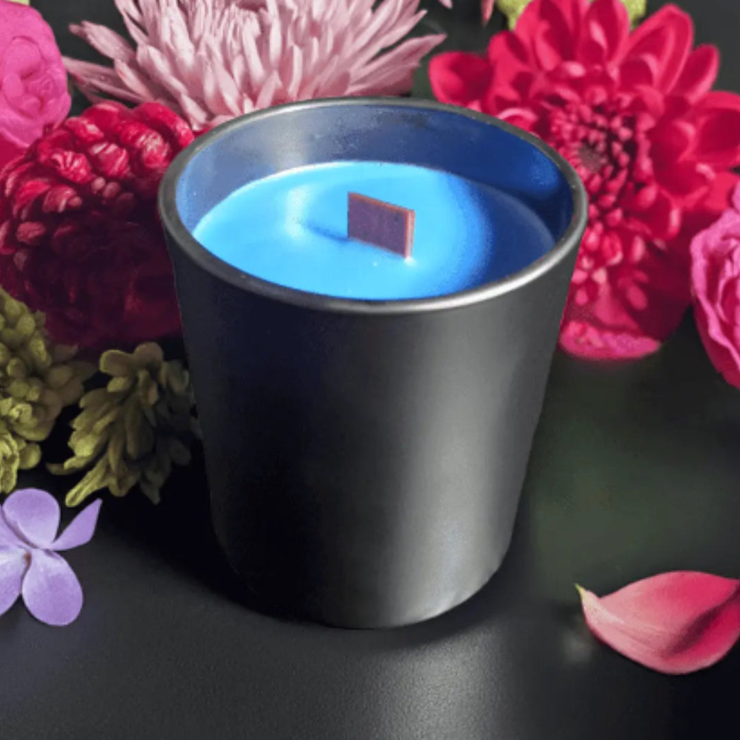 Blue candle in a black container with pink and red flowers on a dark background