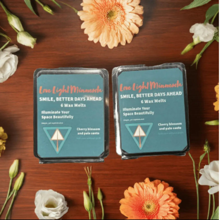 Two packages of 'Love Light Minnesota' wax melts on a wooden surface with flowers around.