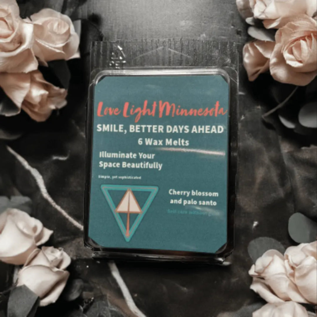 Pack of wax melts with branding and product details, surrounded by flowers on a dark surface