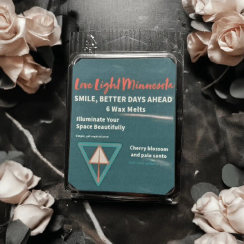 Pack of wax melts with branding and product details, surrounded by flowers on a dark surface