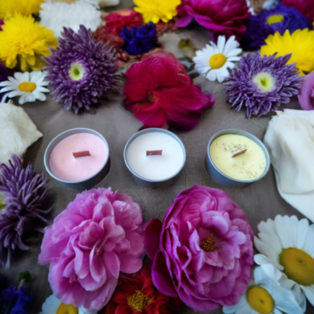 Three small candles surrounded by colorful flowers on a wooden surface