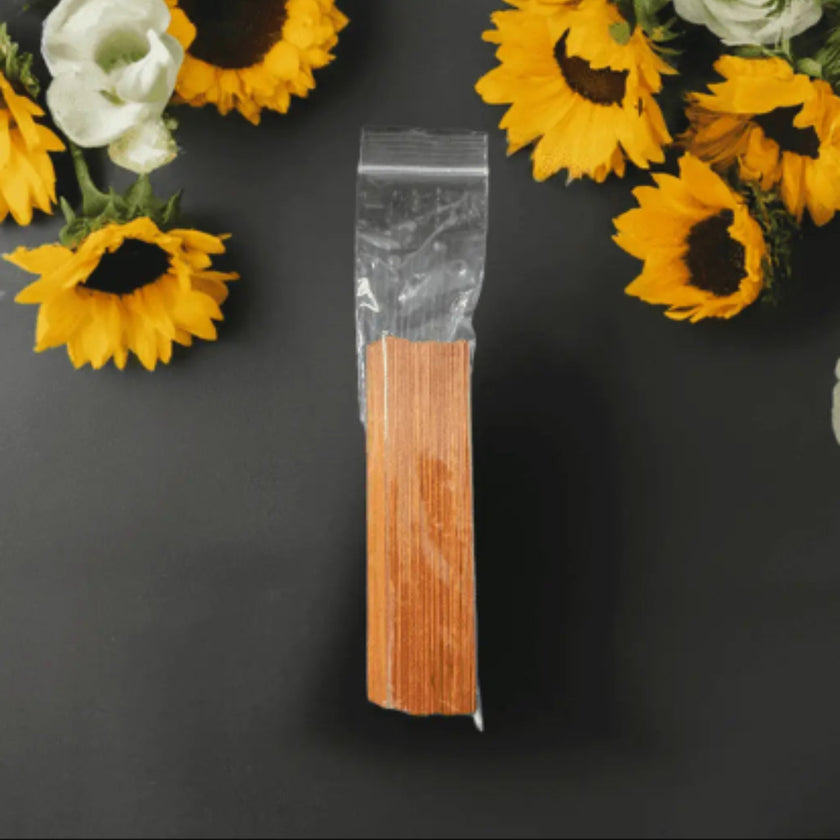 Packaged pre-treated wooden wicks on a dark surface with sunflowers and white flowers.